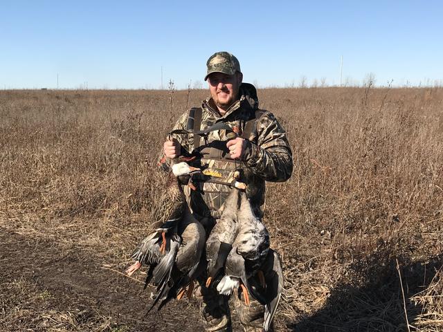Dave holding a strap of ducks in a grass field