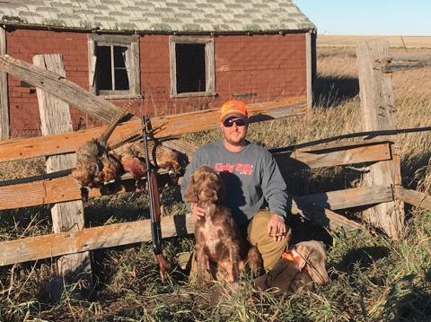Dave and his dog at an old red barn with roosters hung on the fence