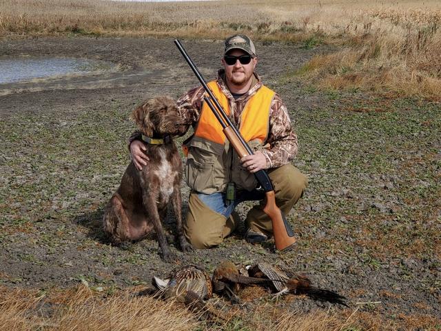 Dave kneeling with his dog and a shotgun, a limit of rooster pheasants in front