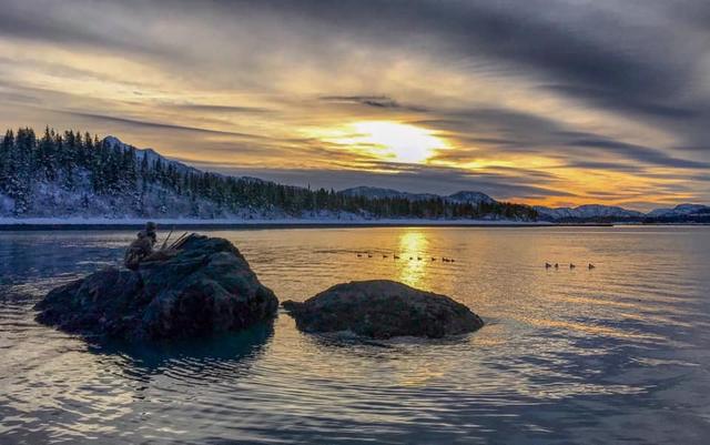 Sunrise over calm water and rocks with ducks on the water
